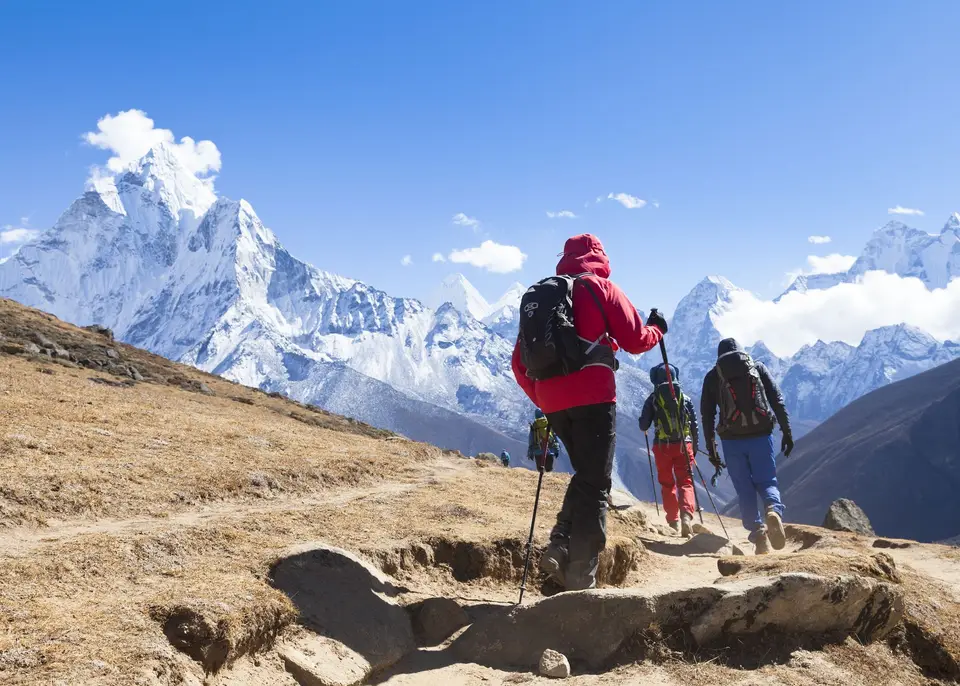 Trekkers following a guide along a rocky trail towards snow-capped mountains