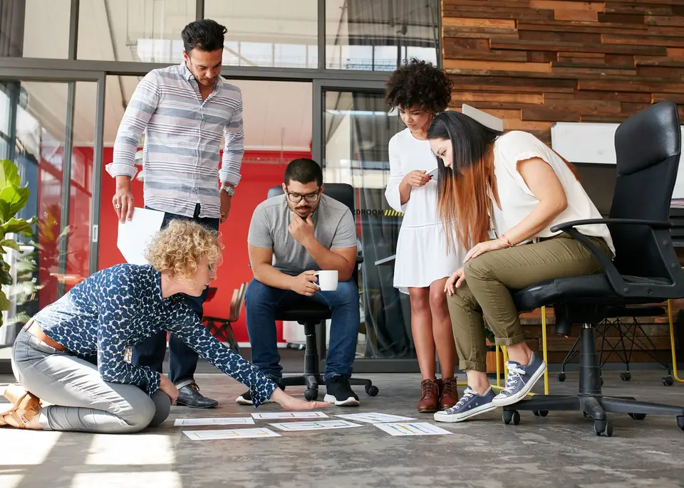 A team gathered around notes laid out on an office floor, working through a plan